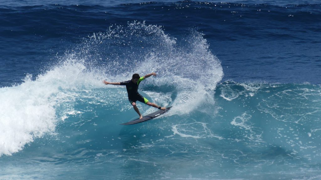 Surfer carving a sharp turn on a black Ekahi surfboard, throwing spray