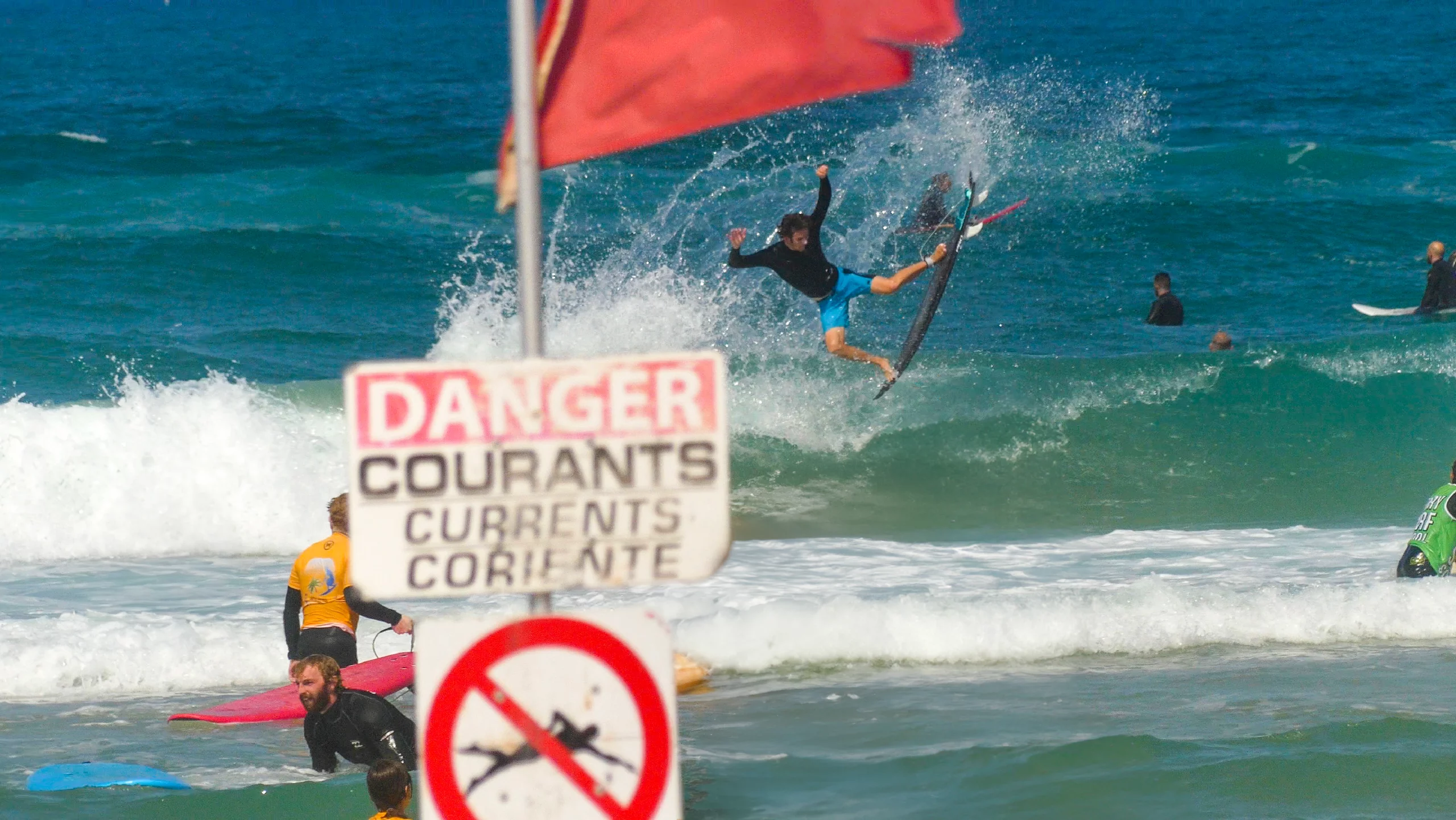 View of a man making an air with a Ekahi Squash carbon surfboard behind a red flag