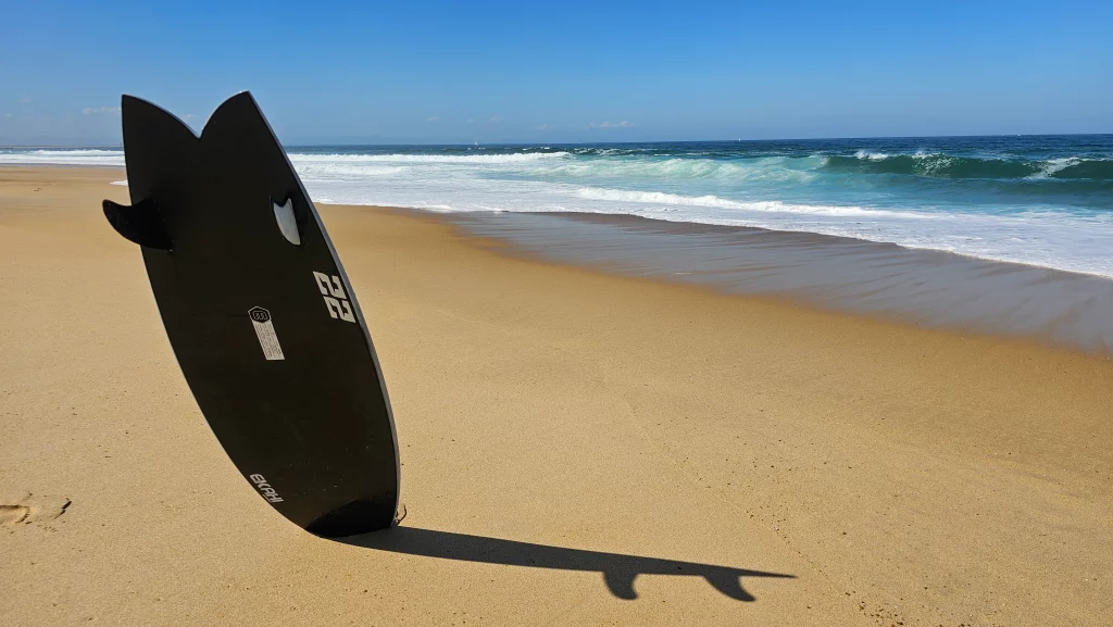 Bottom view of the Ekahi twin fish 22 pearl white carbon surfboard in front of waves