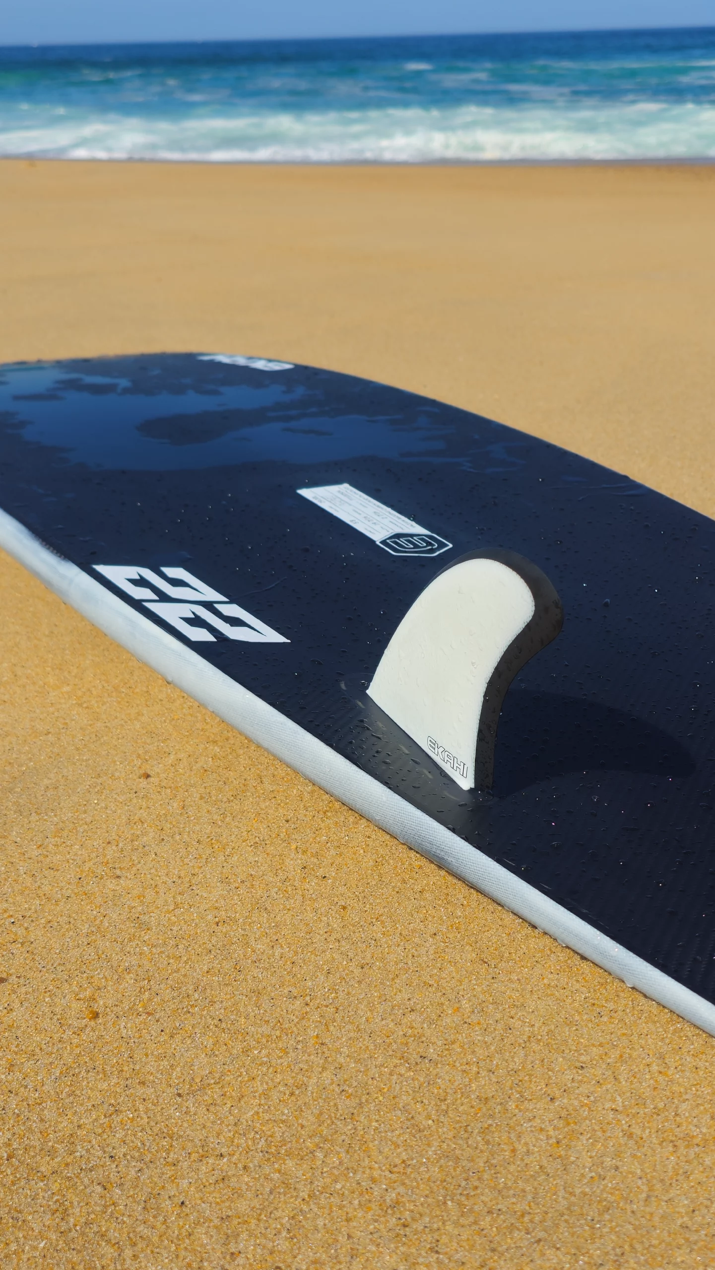 Bottom view on the beach of the twin fish 22 pearl white carbon surfboard with Ekahi twin fins