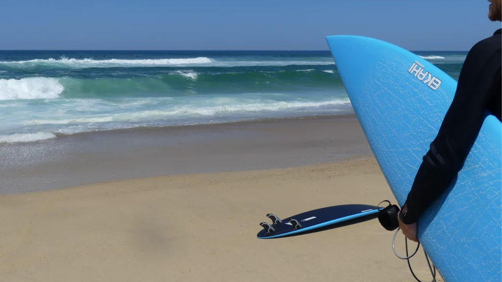 Ekahi Channels 53 carbon surfboard, blue deck, lifestyle photo on the beach