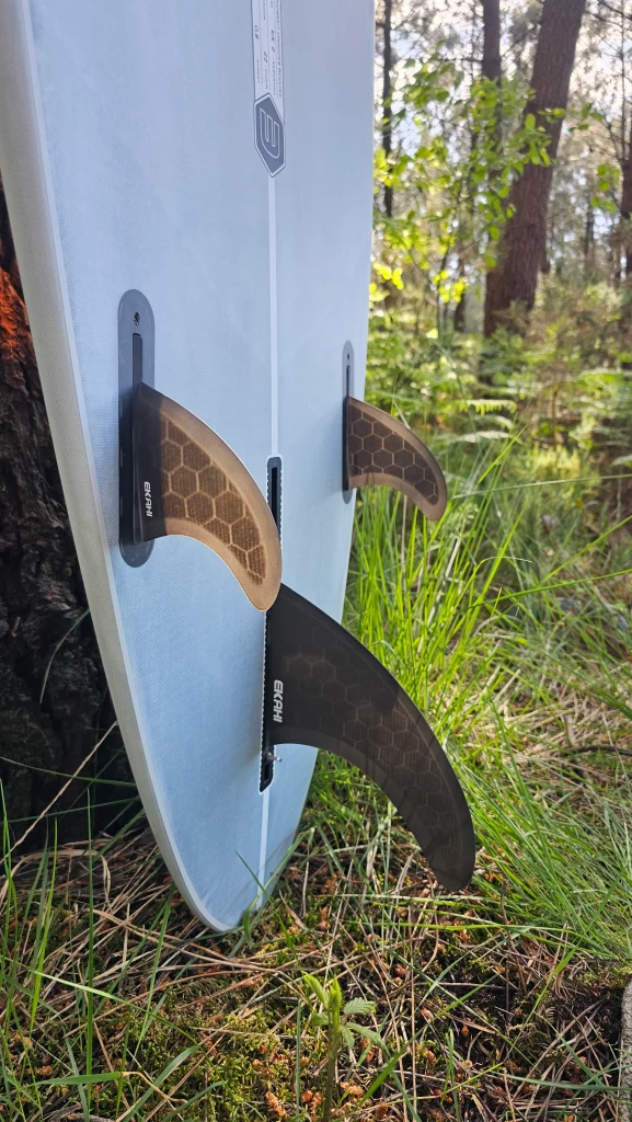 Close-up of the Ekahi fin setup on a Long surfboard, standing in a forest clearing