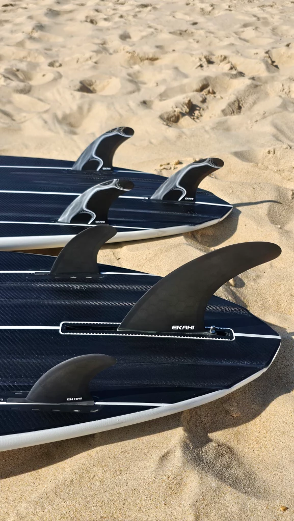 Ekahi Mid carbon surfboards lying on the beach, close-up of the fins