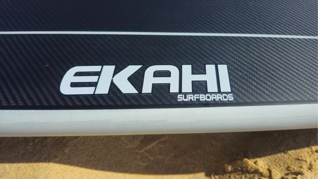 Close-up of the Ekahi Surfboards logo on the rail of a black carbon board