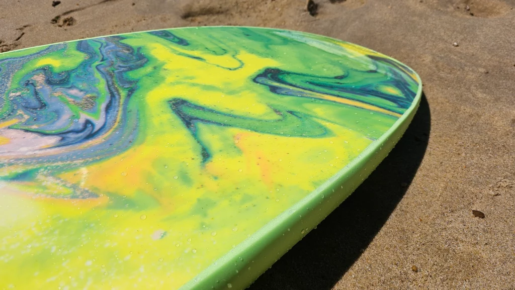 Close-up of a green, yellow and blue marbled Ekahi soft-top surfboard rail