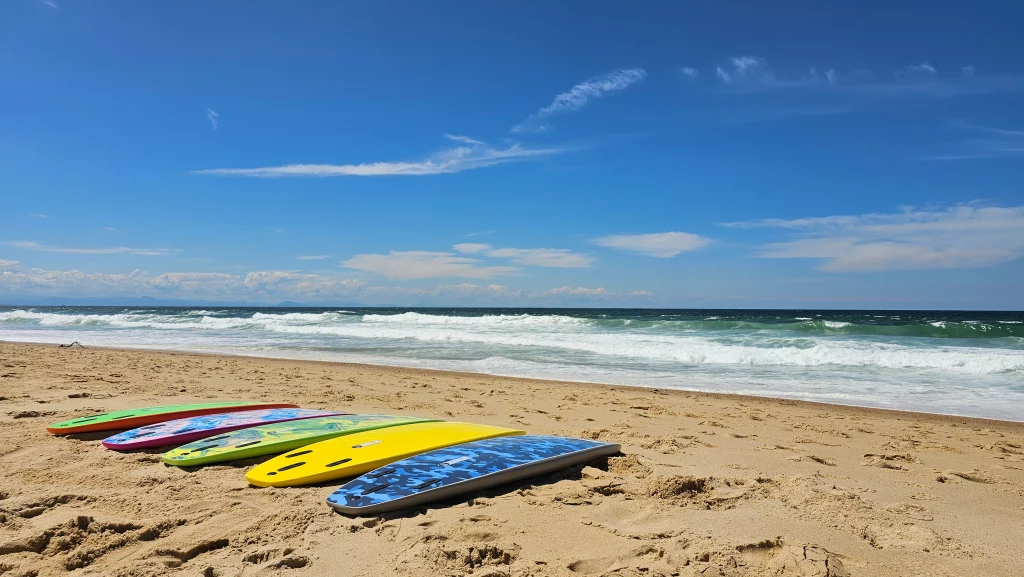 Five Ekahi soft-top surfboards in green, tie-dye, yellow and blue camo lined up on the beach at sunny weather