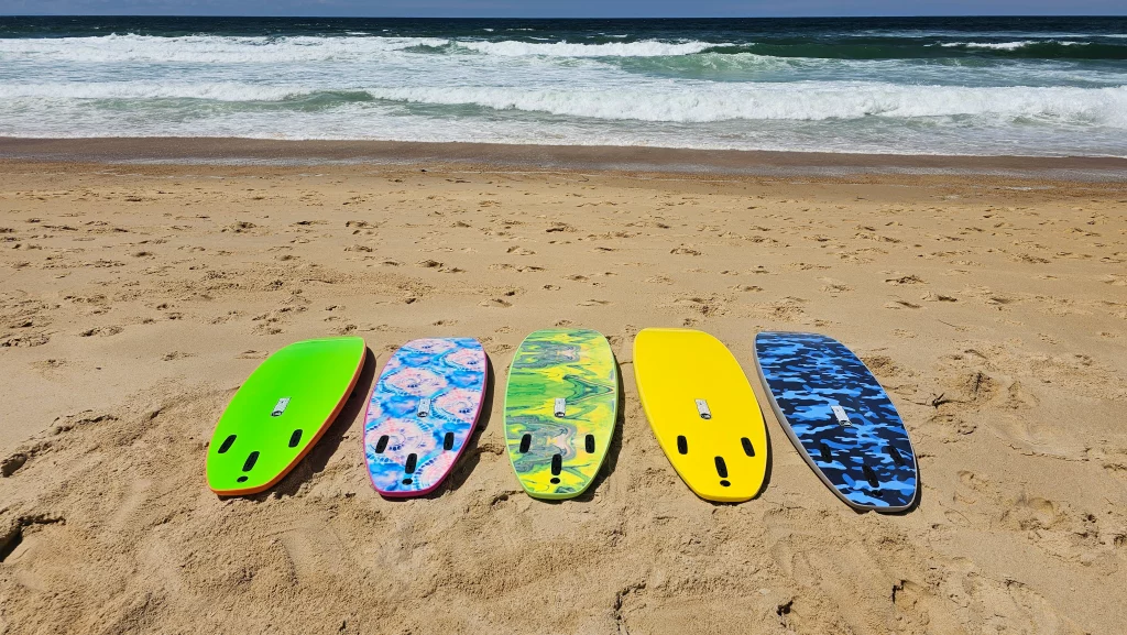 Five Ekahi soft-top surfboards in green, tie-dye, marble, yellow and blue camo lined up facing the ocean