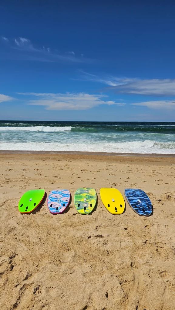 Five Ekahi soft-top surfboards in assorted colors and patterns lined up on the beach, nose view