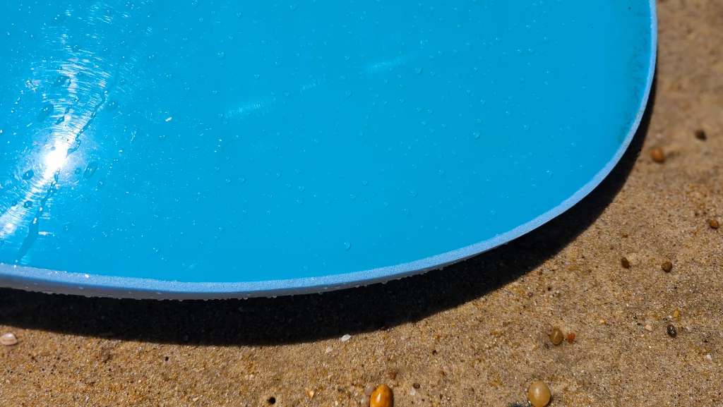 Close-up of the rounded nose rail of a blue Ekahi soft-top surfboard on the sand