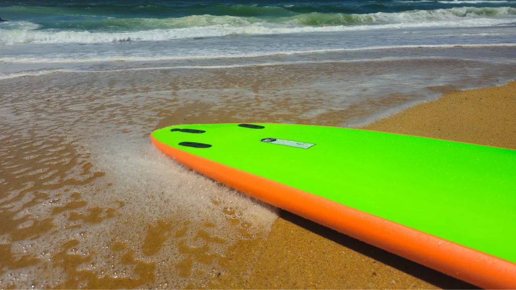 Nose close-up of a green and orange Ekahi soft-top surfboard at the water's edge