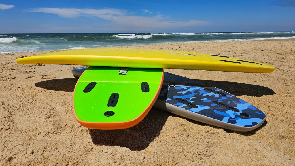 Stack of Ekahi soft-top surfboards in yellow, green and blue camo on the beach