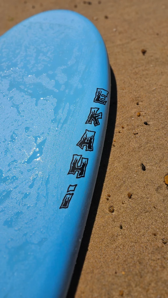 Close-up of the Ekahi logo on the rail of a blue soft-top surfboard
