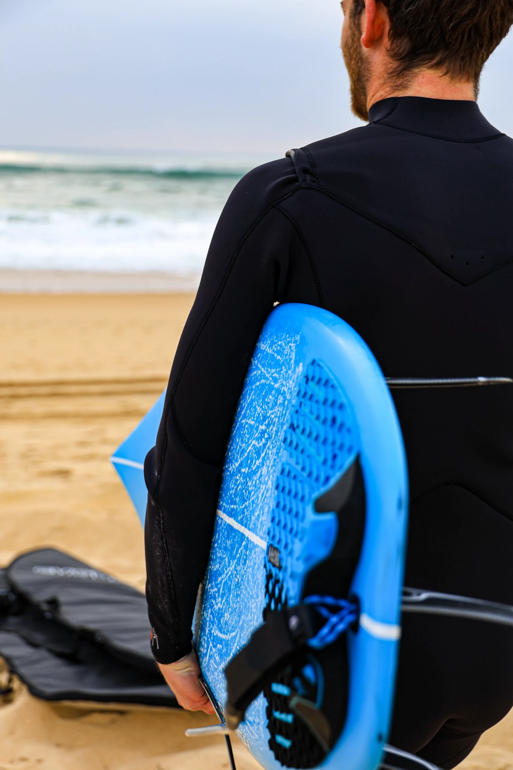 Surfer with the blue carbon Squash surfboard with a round bleu/black grip and a 6ft black/grey leash