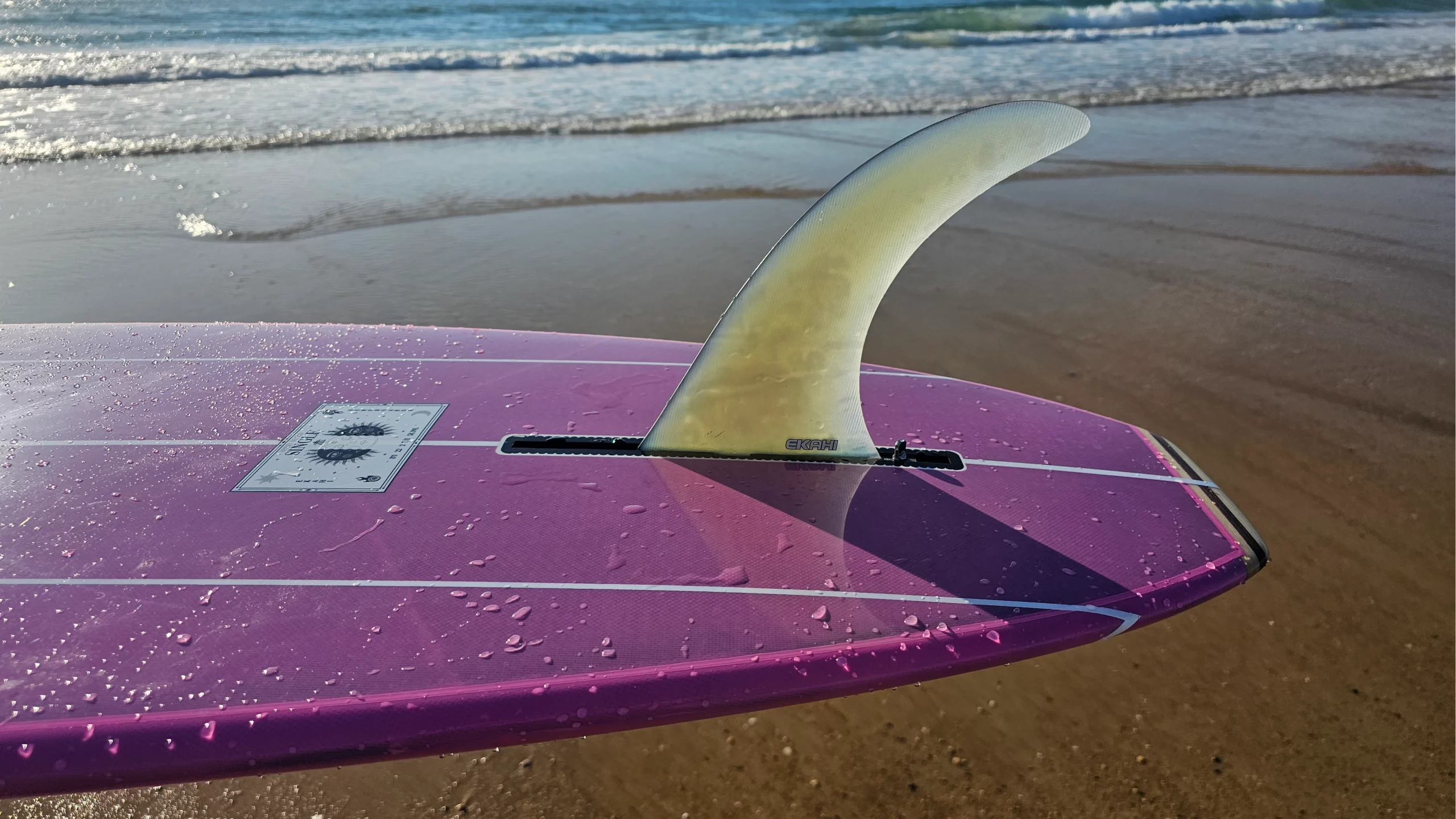 Side view of the Single fin screw on the wood tail of the Ekahi pink longboard.