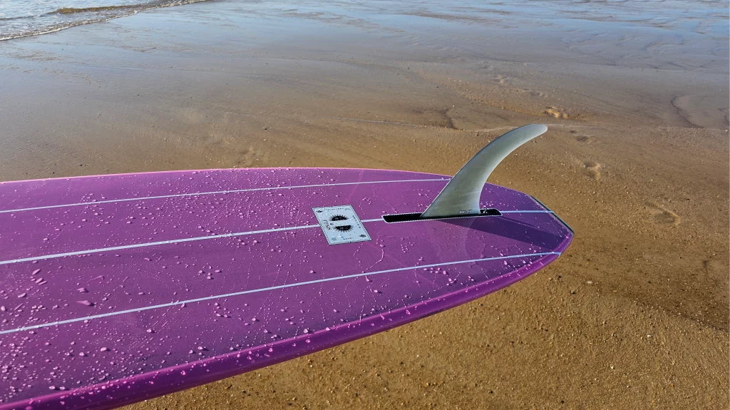 View of the fin near the Single logo on the EKAHI pink classic longboard with pearly water.