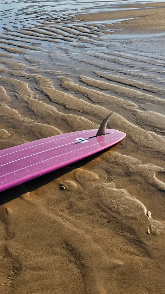 View of the single fin on the EKAHI pink classic longboard on the sand.