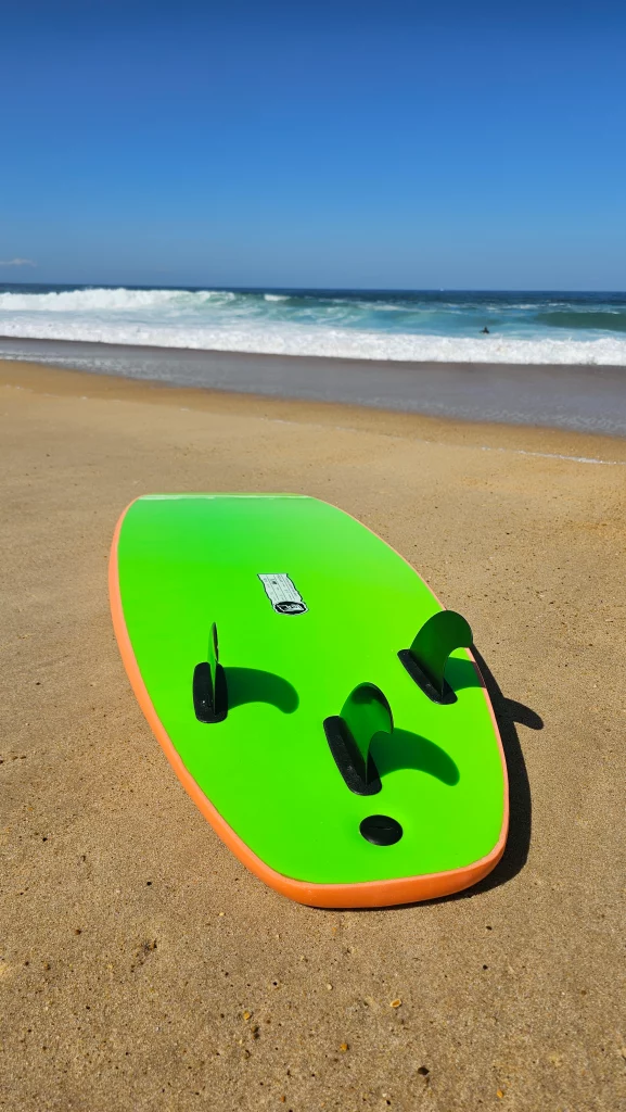 Green and orange Ekahi soft-top surfboard lying on the beach, bottom view with fins