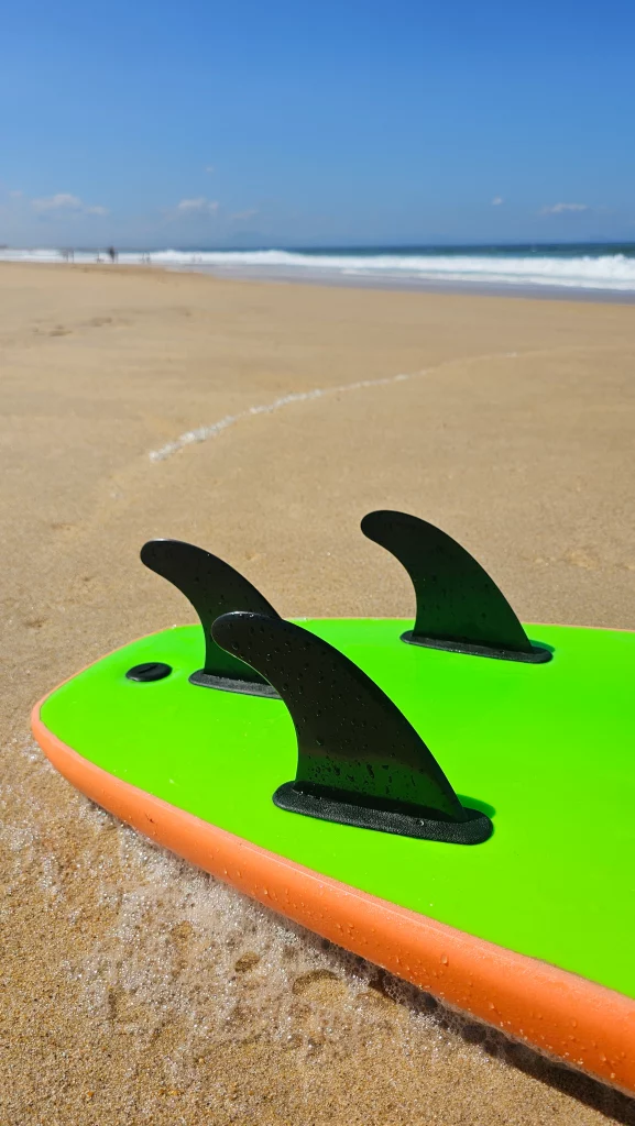 Close-up of the fins on a green Ekahi soft-top surfboard on the beach