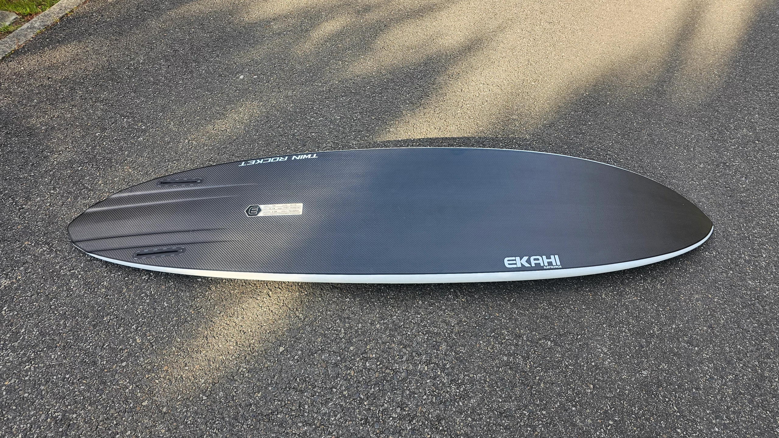 Bottom view of Ekahi white Twin Rocket carbon fiber surfboard with channels and twin fins on the floor.