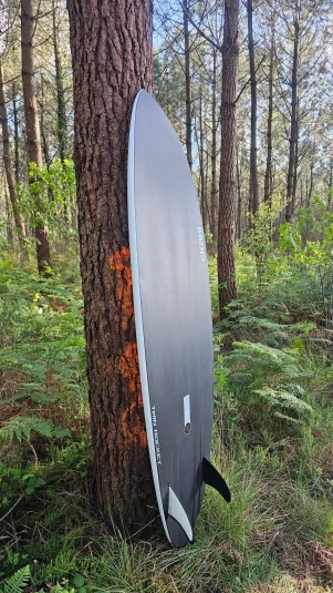 Rail and bottom view of Ekahi white Twin rocket carbon fiber surfboard in the wood forest.