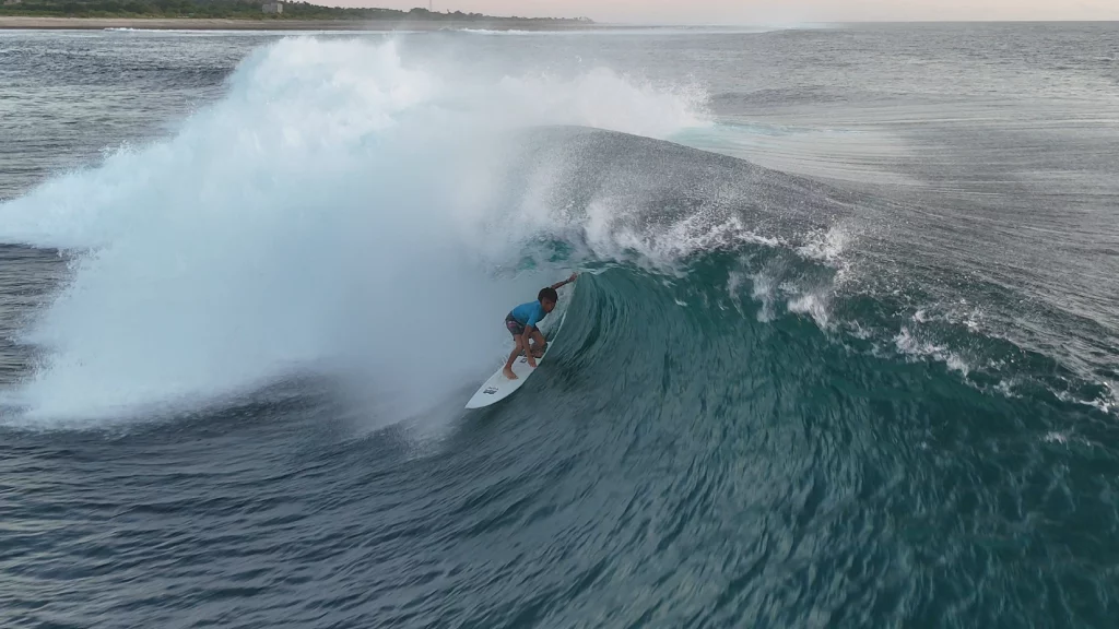 Young ambassador surfer riding deep inside a large barreling wave on a white Ekahi surfboard, aerial drone shot