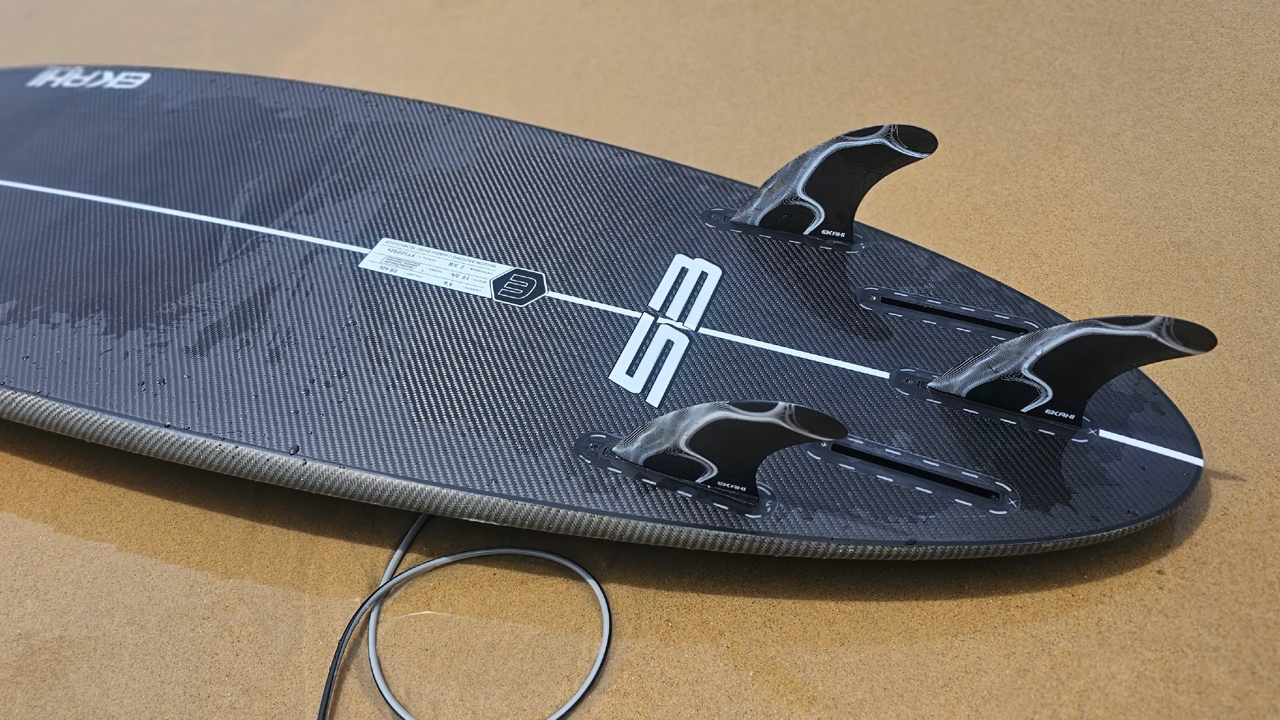 Bottom view of thruster fins fixe on a 53 in carbon kevlar in 5'6 with a black/grey Ekahi surf leash 6ft.