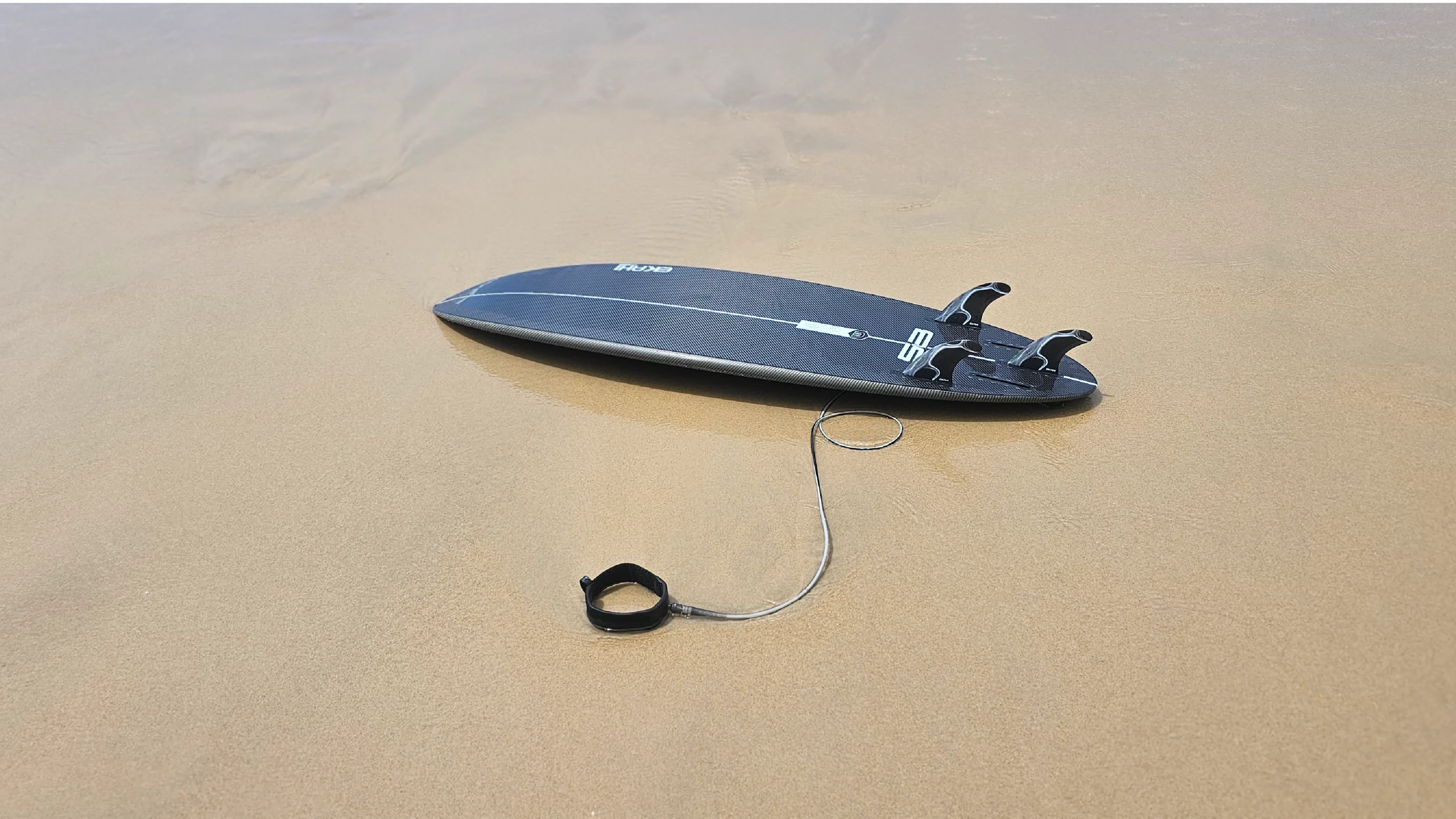 Bottom view of a 53 in carbon kevlar in 5'6 with a black/grey Ekahi surf leash 6ft and thruster fins.