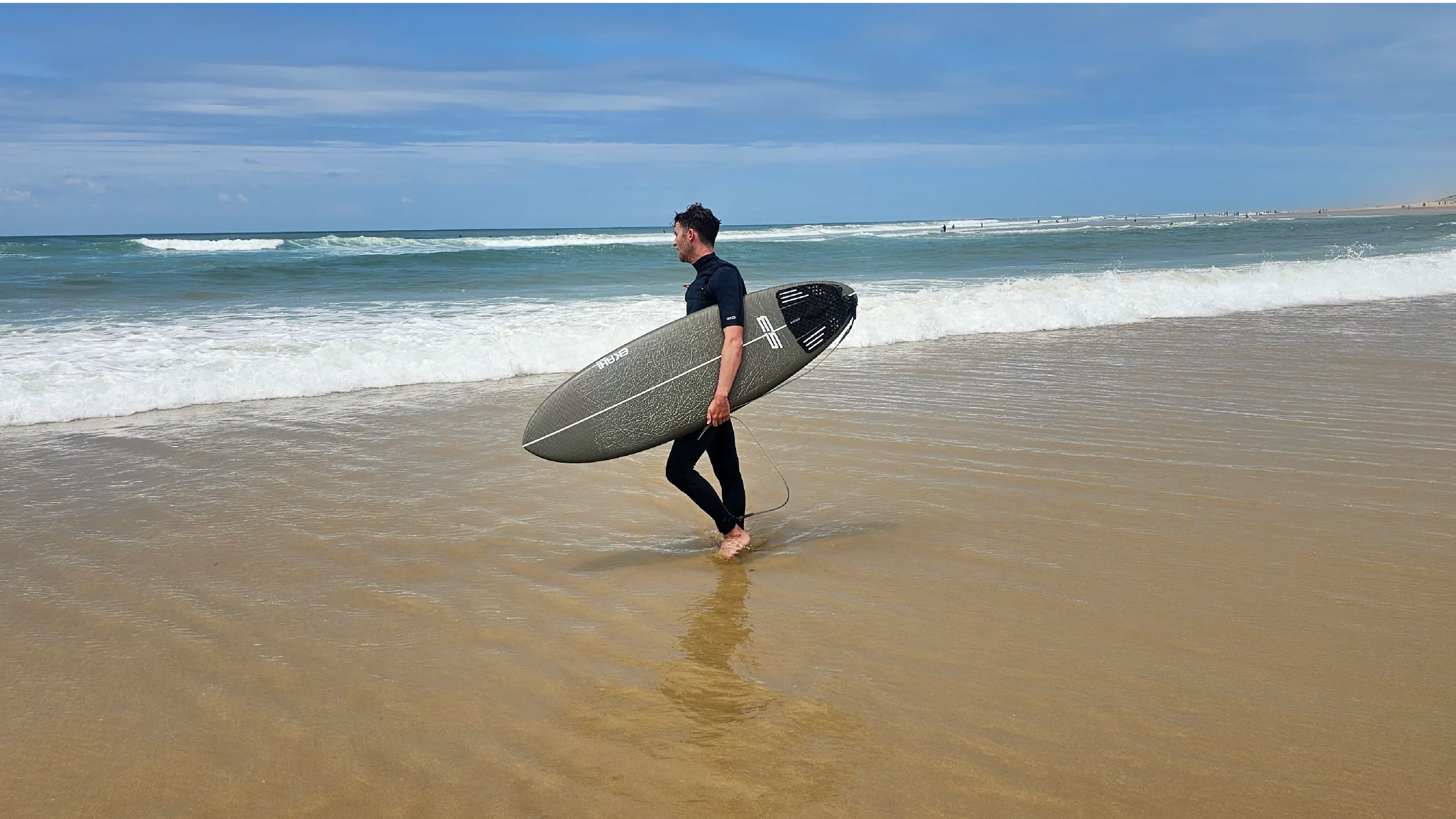 Surfer walking on the beach with a carbon kevlar 53 surfboard in 5'6 with a marble Round traction pad.