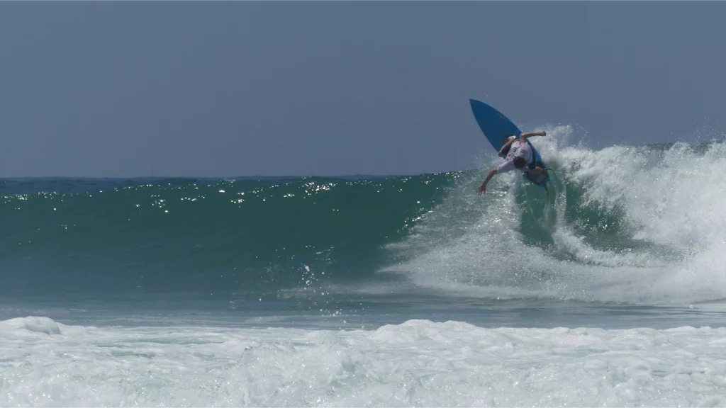 Surfer making a backside roller with a blue color swallow Channels easy-rider surfboard.