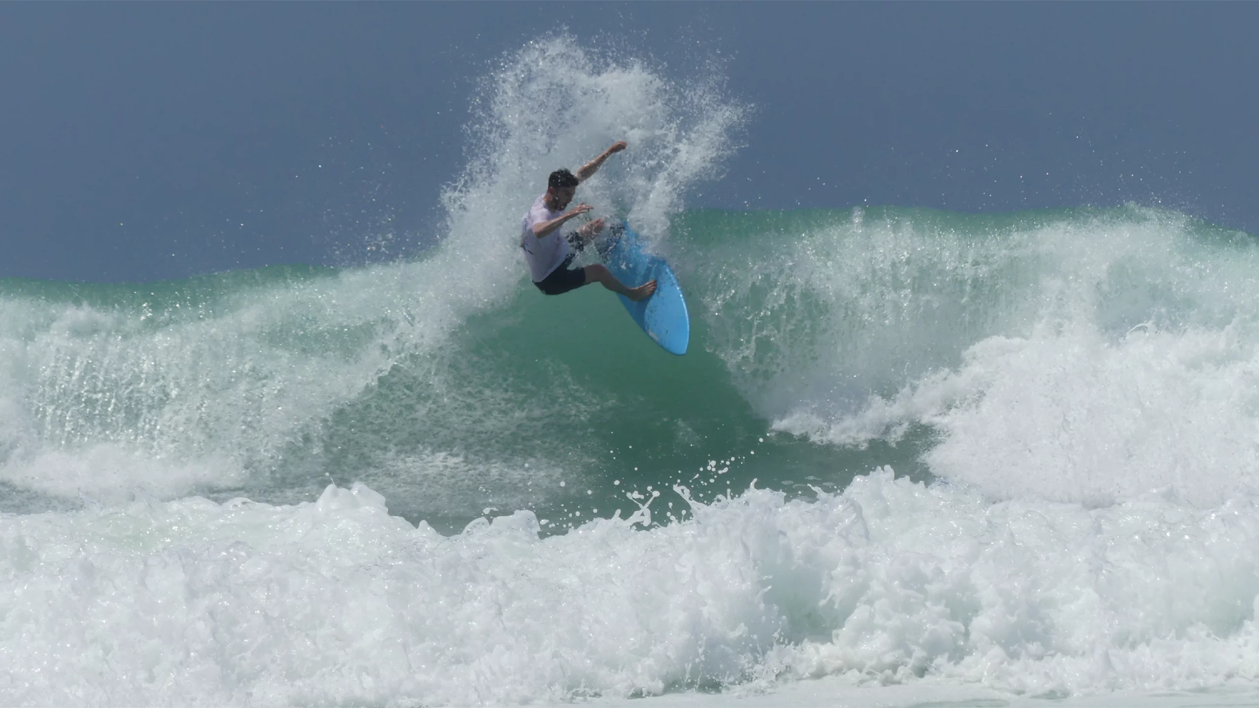 Surfer making a critical roller with a blue carbon Channels surfboards 5'8.