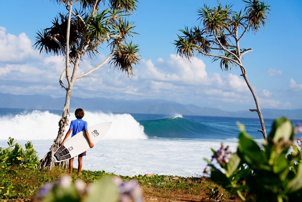 View of a guy looking at a wave with a EKAHI white 5'0 channels carbon surfboard and a grom marble traction pad.