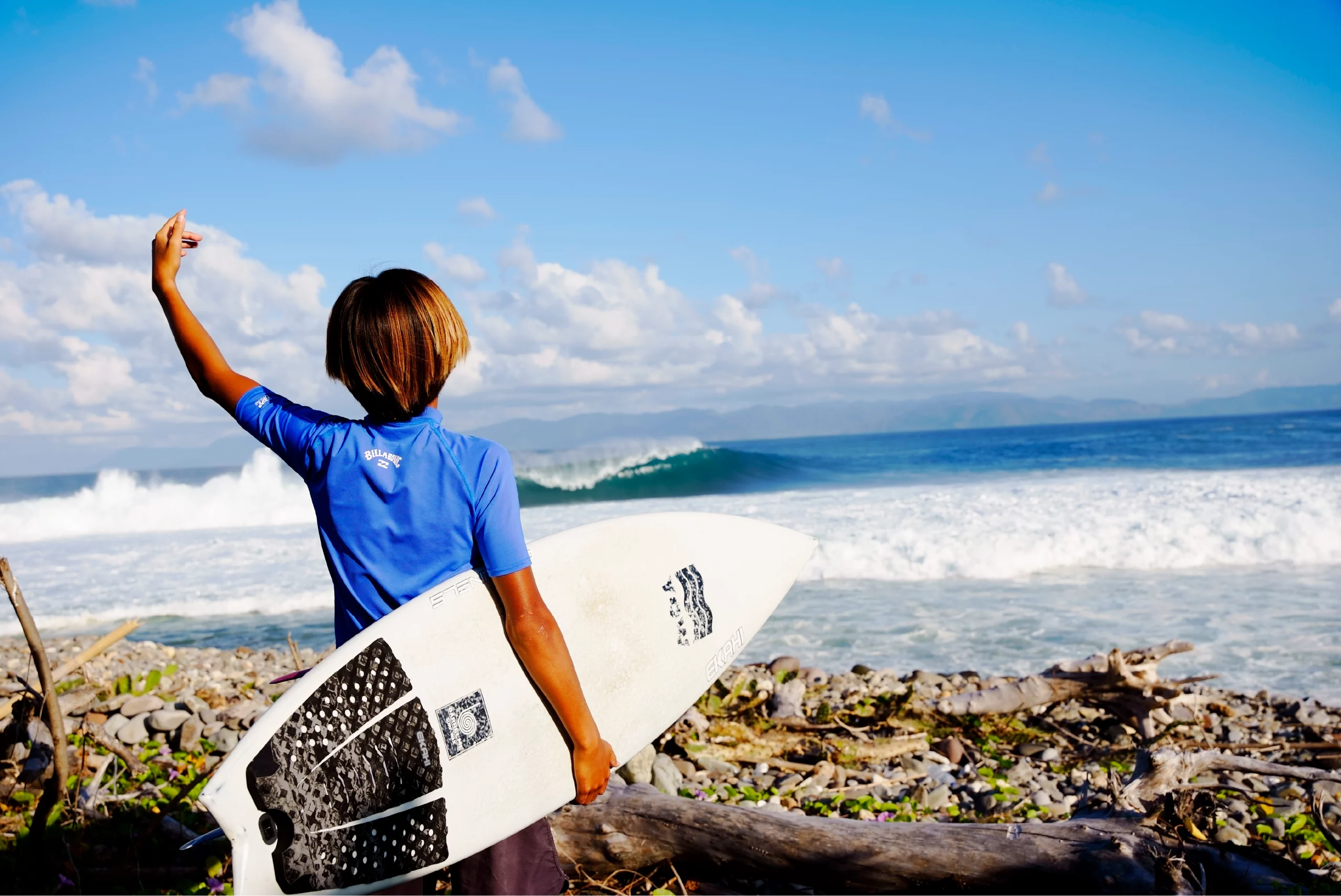 View of a guy smiling with a white 5'0 channels carbon surfboard and a grom marble traction pad.