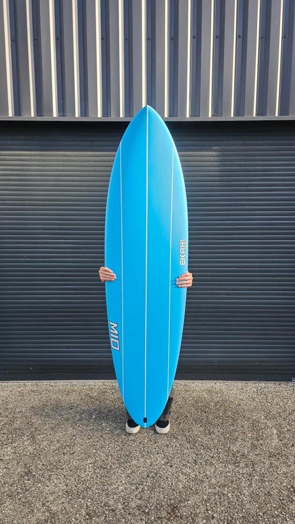 Ekahi Mid carbon surfboard, blue deck, top deck view, held by hand for scale