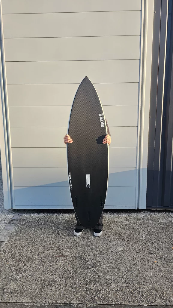 Ekahi Squash carbon surfboard, white deck, bottom view, held by hand for scale