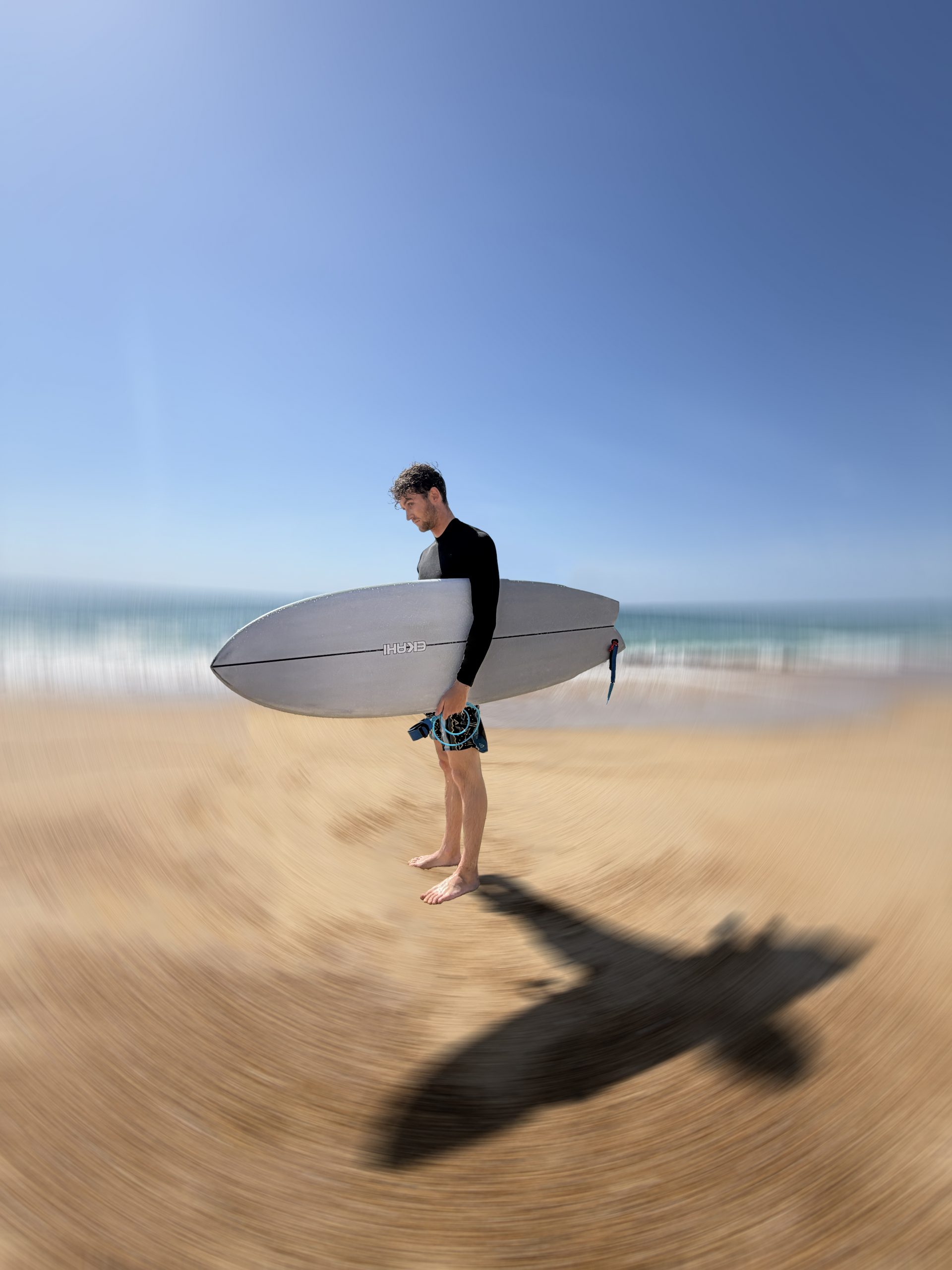 Surfer walking on the beach carrying an Ekahi carbon surfboard, motion-blur lifestyle photo